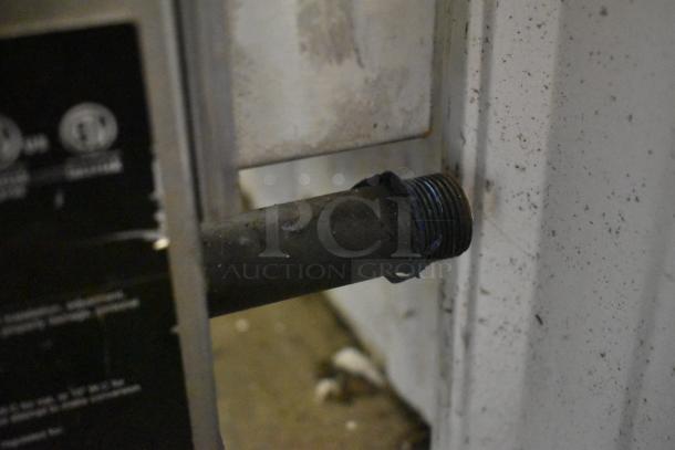 Close-up of a threaded metal pipe protruding from a white wall. Black label partially visible with unreadable text. Slight wear.