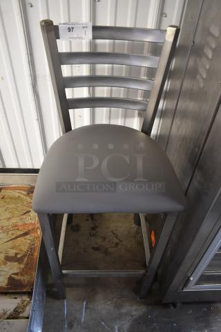 Metal chair with horizontal backrest bars, gray cushioned seat, auction tag labeled "97". Sturdy condition, ideal for dining.