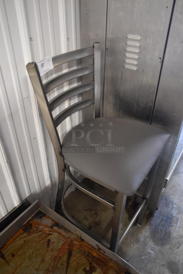 Metal bar stool with gray cushioned seat and ladder back design, in good condition. Auction tag labeled "97" attached.