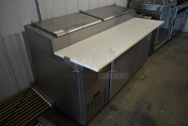 Stainless steel commercial prep table with dual doors and cutting board, ventilated panel, handle lids on top, used condition.
