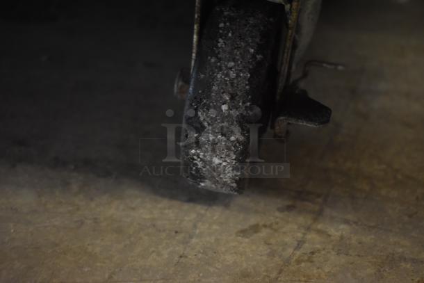 Close-up of a worn industrial caster wheel on a rough floor, showing corrosion and dirt buildup, indicating heavy use.