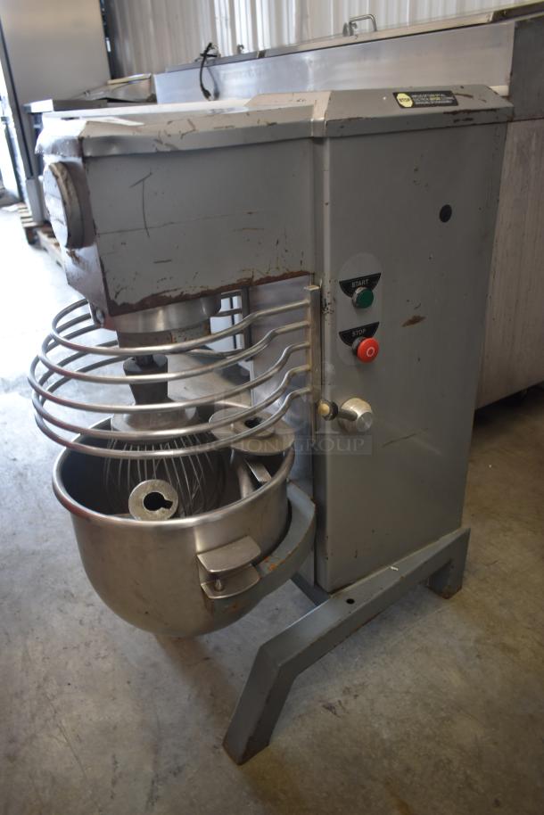 Commercial industrial mixer with metal bowl, wire guard, and start/stop buttons; shows signs of wear and use.