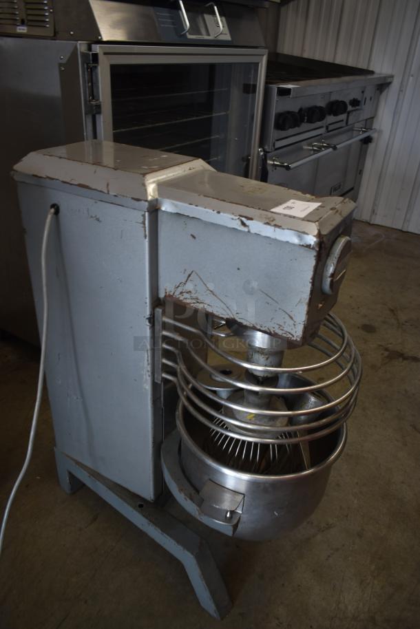 Industrial dough mixer with stainless steel bowl, showing signs of wear, includes attached label.
