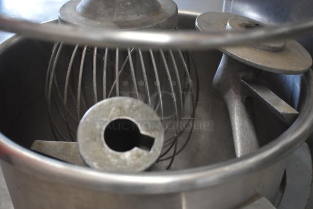 Industrial dough mixer with metal whisk and paddle attachments in stainless steel bowl, slightly used condition.