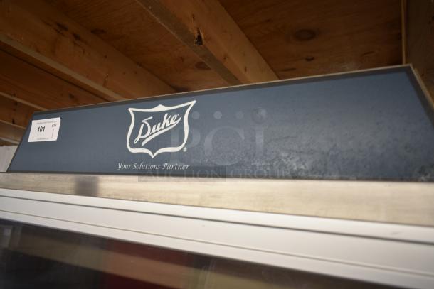 Duke branded equipment, labeled "Your Solutions Partner," auction tag 101, displayed under wooden shelving.