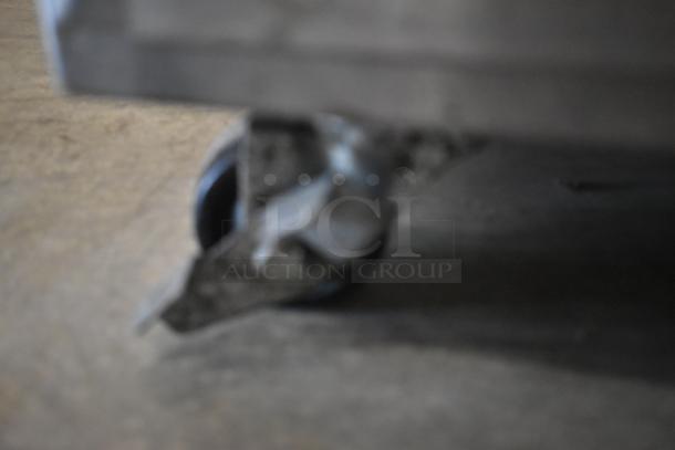 Blurry image of a caster wheel attached to a metal frame on a concrete floor. Condition unclear.