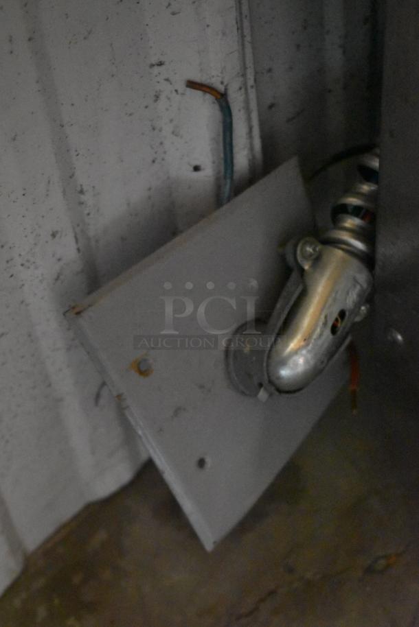 Metal wall bracket with attached caster wheel, showing exposed wiring. Some rust present, indicating wear.