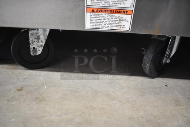 Metal equipment base with black caster wheels, showing slight wear. Warning labels in French above wheels.