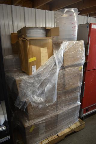 Pallet of stacked cardboard boxes wrapped in plastic, with clear plastic containers on top marked with liter measurements.
