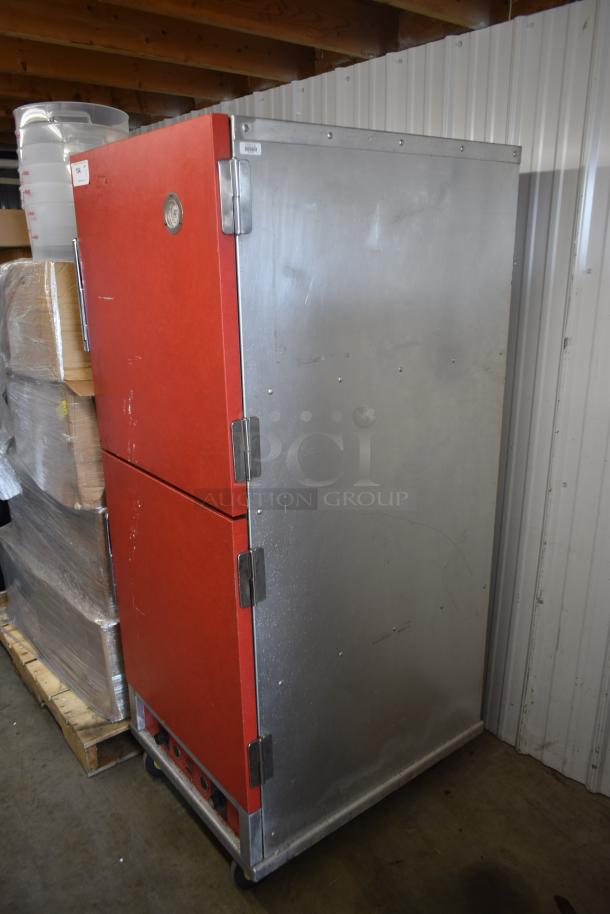 Commercial red and stainless steel warming cabinet with dual doors, thermometer, and wheels. Used condition, some surface wear.