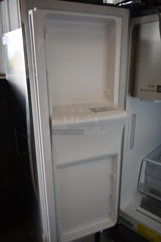 Open refrigerator door interior with empty white shelves, featuring an ice maker on the right side. Appears in good condition.