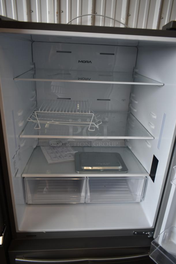 Mora stainless steel refrigerator interior with adjustable shelves, wire rack, and two transparent drawers. Appears unused.