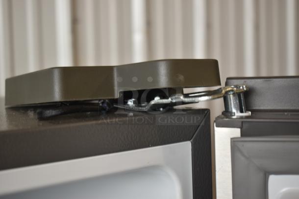 Close-up of a metal latch mechanism on a gray appliance in good condition. Features a black cover and secure fastener.