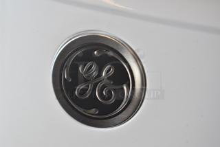 GE logo emblem on a white appliance surface, featuring metallic finish and engraved detailing, suggesting brand authenticity.