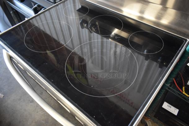 Stainless steel electric stove with smooth glass cooktop, five burners, and minimal wear. Model label reads "Frigidaire."