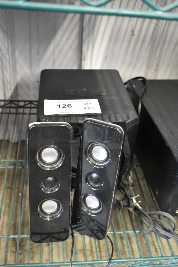 Black three-piece speaker system with subwoofer and two satellite speakers. Auction tag "126 VX3" attached. Used condition.