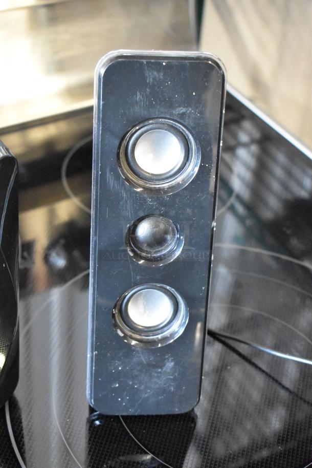 Black desktop speaker system with three circular speaker cones. Minor surface scratches visible.