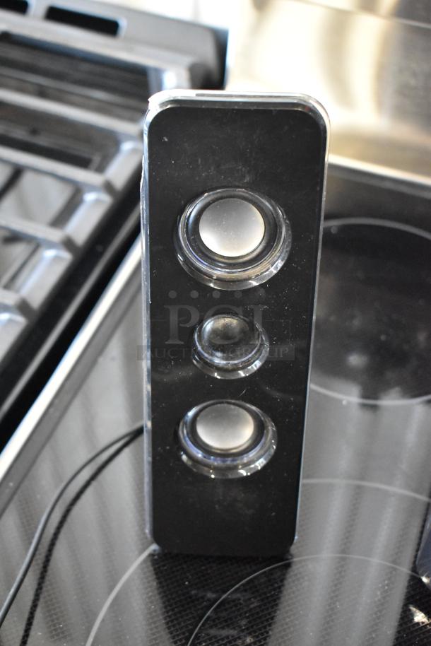 Black rectangular speaker with three circular drivers, glossy finish, visible surface scratches indicating use.