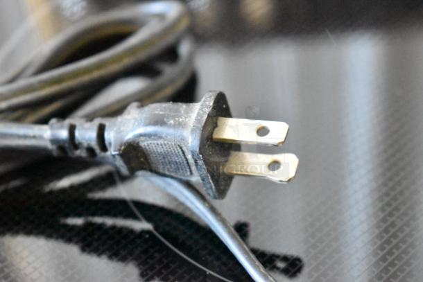 Two-prong plug with black rubber cord, slightly dusty, laying on a reflective surface. No visible labels or markings.