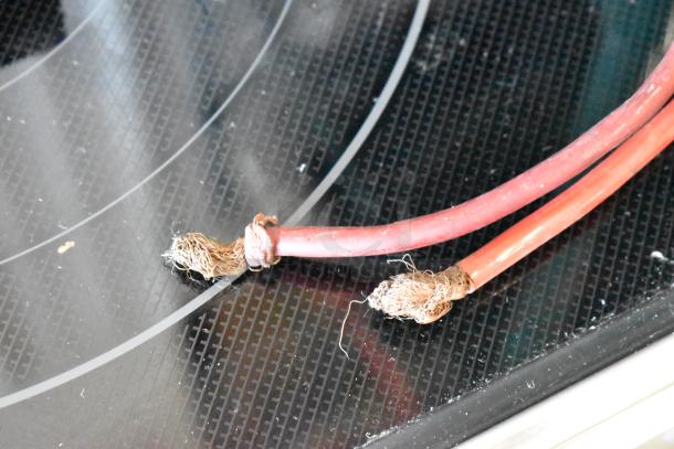 Frayed red electrical cables with exposed copper wires on a glass-ceramic cooktop surface.