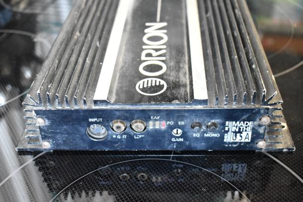 Orion car amplifier, black with silver accents, shows signs of wear. Features input control, gain knob, and "Made in USA" label.