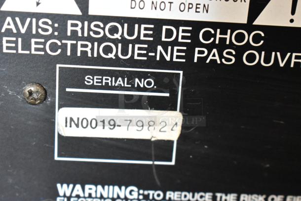 Serial number label on electronic device, reads "IN0019-79824." Warning text: "Risk of electric shock. Do not open."