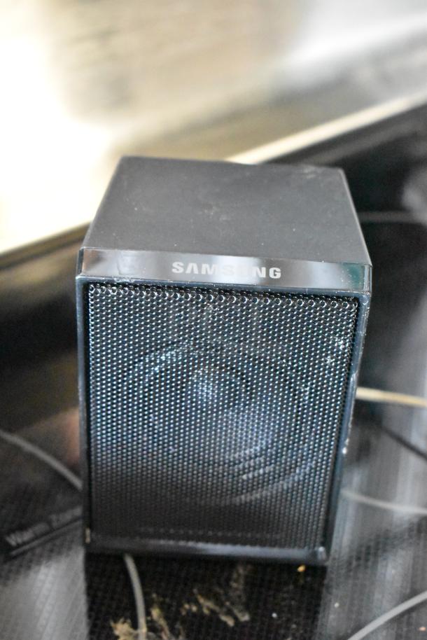Samsung black desktop speaker, rectangular design, metal grille front, visible brand logo, power cord attached, good condition.