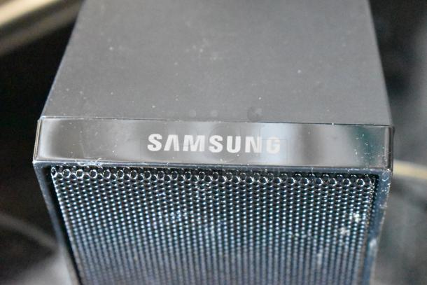 Samsung speaker with black mesh grille, slightly worn. Prominent "Samsung" logo on top edge. Suitable for audio systems.