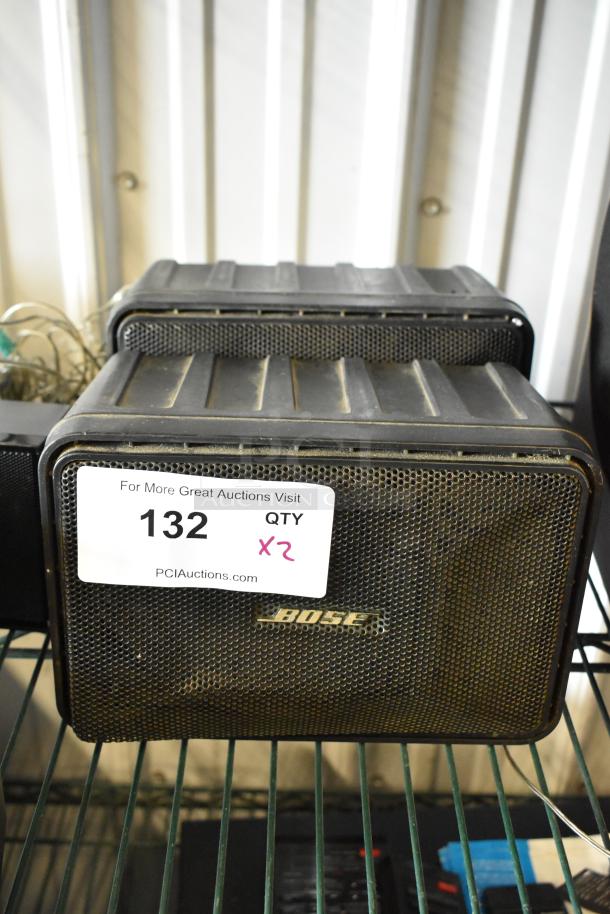 Pair of Bose speakers in used condition, marked with auction tag showing number 132 and quantity 2.