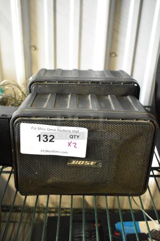 Pair of Bose speakers in used condition, marked with auction tag showing number 132 and quantity 2.