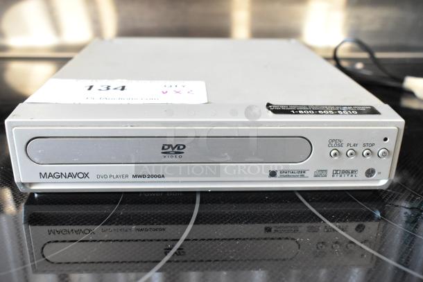Magnavox DVD Player MWD200GA, silver, features Spatializer and Dolby Digital. Auction tag 134 visible. Minor wear.
