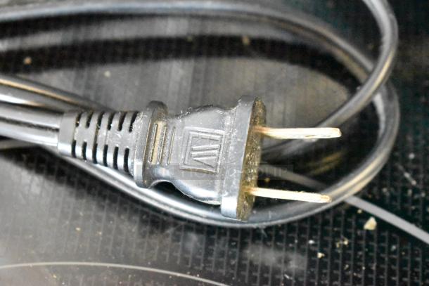 Black two-prong power cord with textured grip, minor wear visible, geometric logo imprint on the plug.