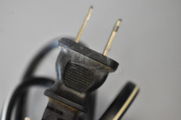 Close-up of a used black power cord with a two-prong plug, showing signs of wear.