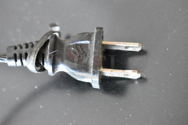 Black electrical plug with two metal prongs, coiled cord, and embossed hand symbol. Used condition.