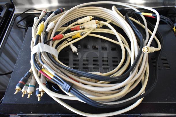Bundle of mixed RCA audio-video cables with various colored plugs, used condition, coiled on a black surface.