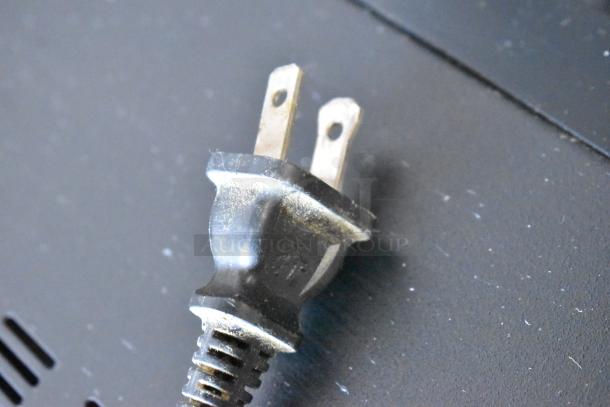 Close-up of a two-prong electrical plug, slightly worn, black plastic housing with visible scratches, no labels visible.