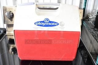 Red Igloo Playmate cooler, white lid with handle, blue logo. Shows signs of wear. Ideal for travel or picnics.