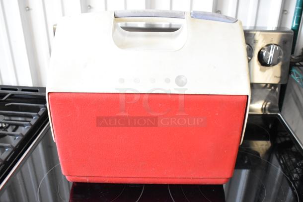 Red and white vintage cooler with handle, showing signs of wear. Ideal for outdoor use or as a collectible item.