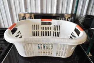 White plastic laundry basket with red handles, open grid design, showing signs of wear. Visible label with product details.