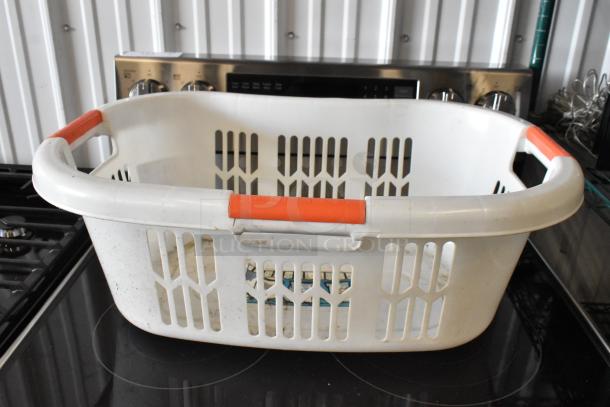 White plastic laundry basket with red handles, showing signs of wear and slight dirt. No tags or labels visible.