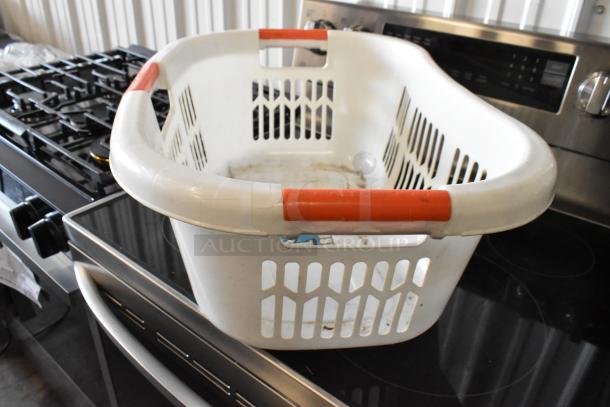 White plastic laundry basket with red handles, used condition, showing wear and dirt inside, placed on a stove.