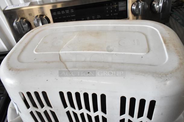 White plastic laundry basket with lid, showing visible dirt and wear, marked "124" on edge, placed on a stove top.