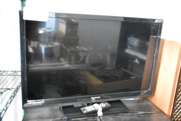 Flat-screen Sylvania TV with remote, reflective screen, mild wear on edges. Auction tag visible, suggesting item number.