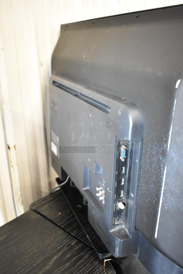 Rear view of a black flat-screen TV showing various input ports, including HDMI and VGA. Moderate wear visible.