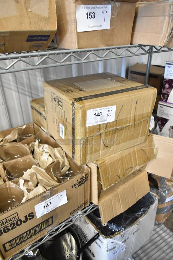 Stacked cardboard boxes on metal shelf with auction labels; contains glassware and kitchen items. Boxes marked "Libbey 3620JS."
