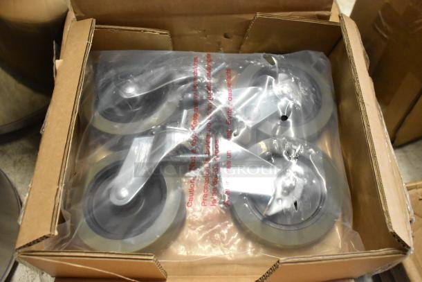 Box of four new industrial caster wheels, packaged in plastic, with metal brackets and rubber tires.