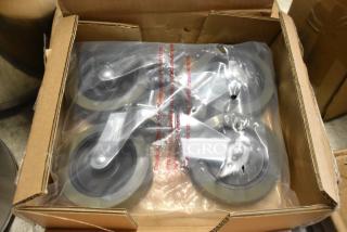Box of four new industrial caster wheels, packaged in plastic, with metal brackets and rubber tires.