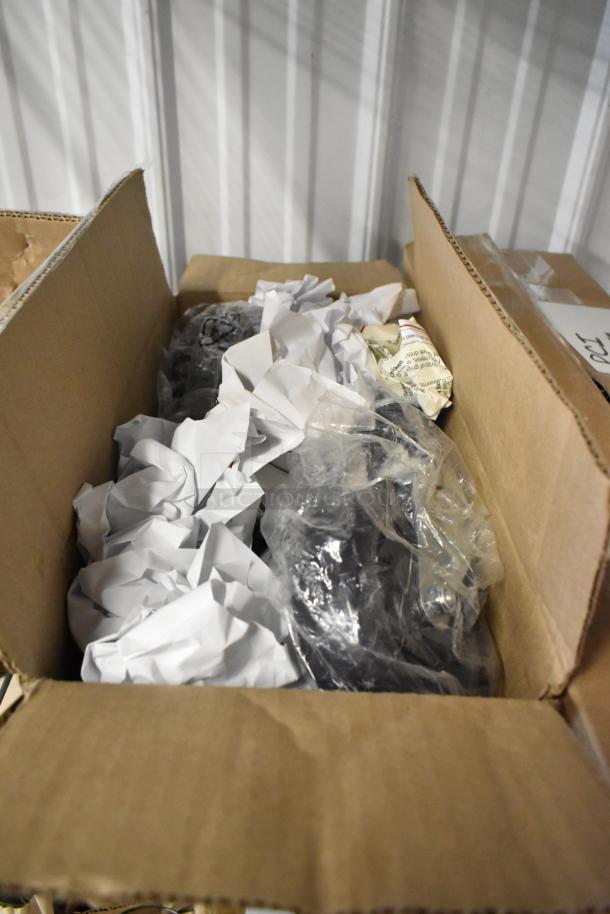 Open cardboard box containing crumpled paper and plastic-wrapped items, possibly for shipping or storage. No visible labels.
