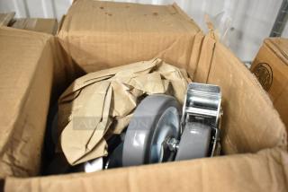 Box containing new gray caster wheels, partially wrapped in brown paper, featuring sturdy metal brackets.