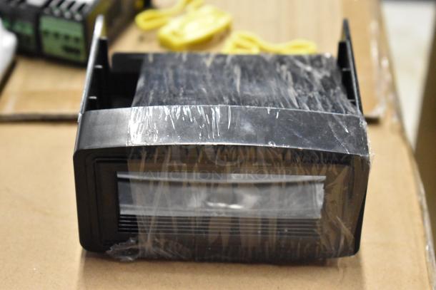 Black electronic device with plastic wrapping, likely a display panel, in new condition. No visible labels or markings.